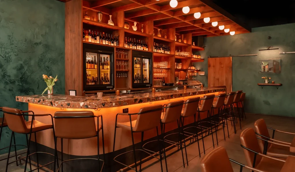 An empty restaurant with a long bar, wood shelves, and green walls.
