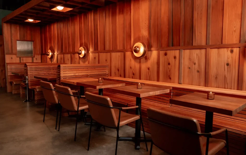 Warmly lit restaurant interior with wooden walls, benches, and tables with candles.