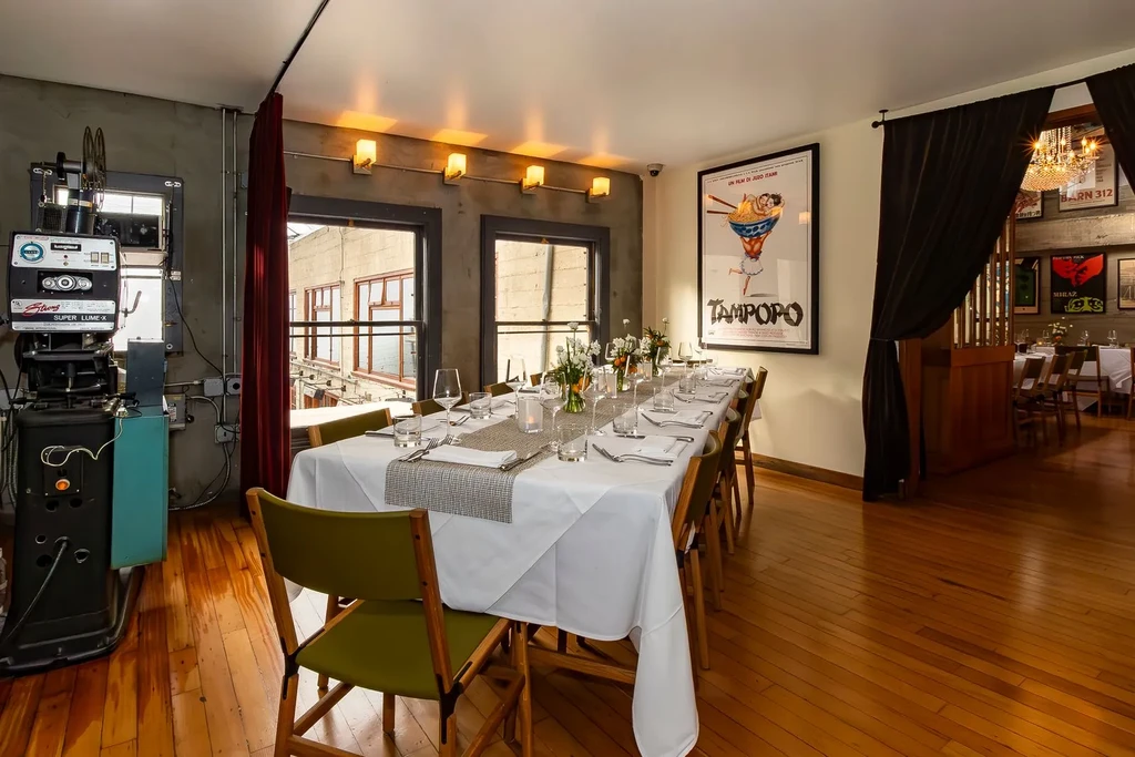 Restaurant dining room with a long table, movie projector, and film poster.