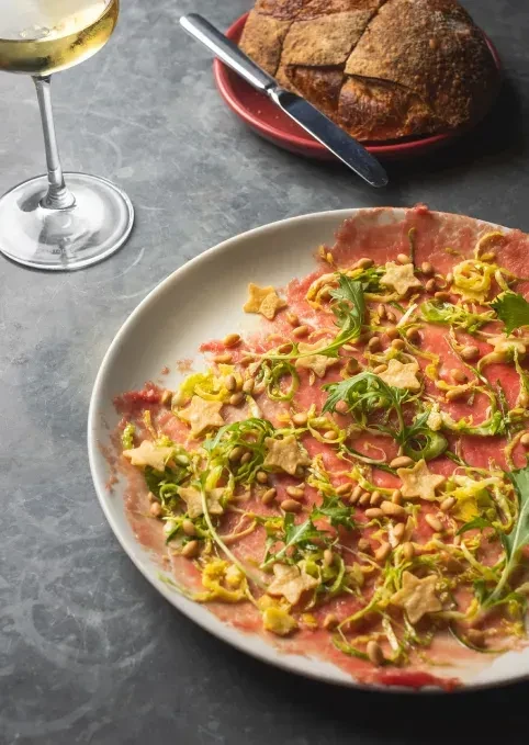 Close-up of a carpaccio dish with wine and bread.