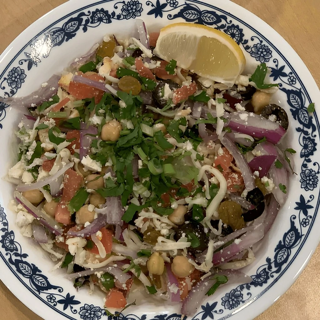 A bowl of chickpea salad with feta, olives, red onion, and lemon.