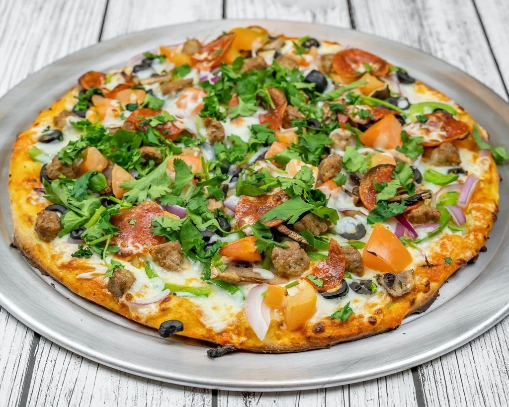 A whole pepperoni, sausage, and vegetable pizza with fresh cilantro.