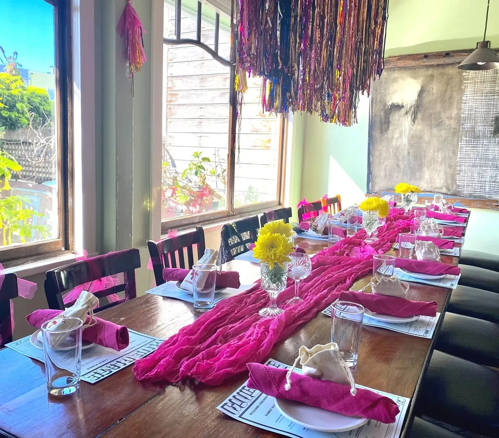 Long dining table set with pink runner, napkins, yellow flowers, and place settings.