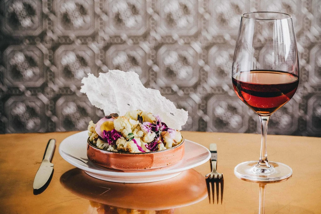 An artistic dish of cauliflower and egg served with red wine.