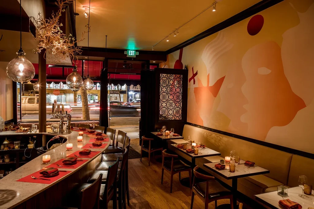 A cozy restaurant interior with bar seating, tables, and a mural.
