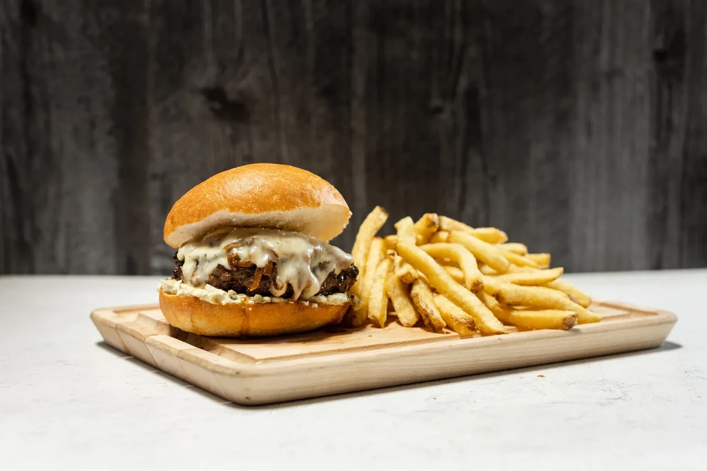Burger with melted cheese and fries on a wooden board.