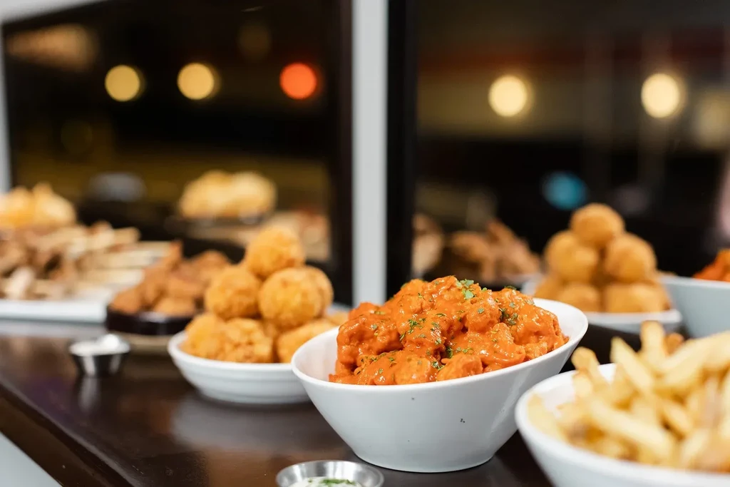Bowls of fried appetizers including orange sauced cauliflower, cheese balls, and fries.