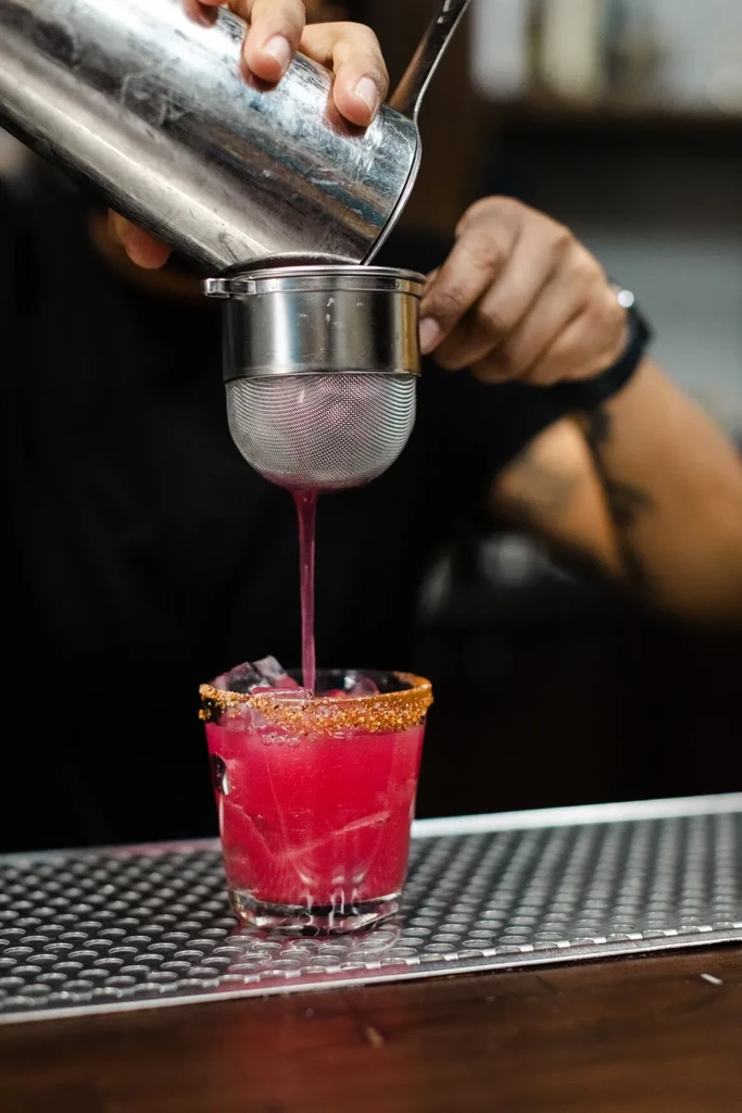 A bartender pours a vibrant pink drink into a glass.