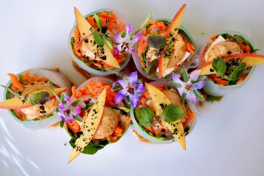 Overhead view of six fresh spring rolls with edible flowers and sliced apple.