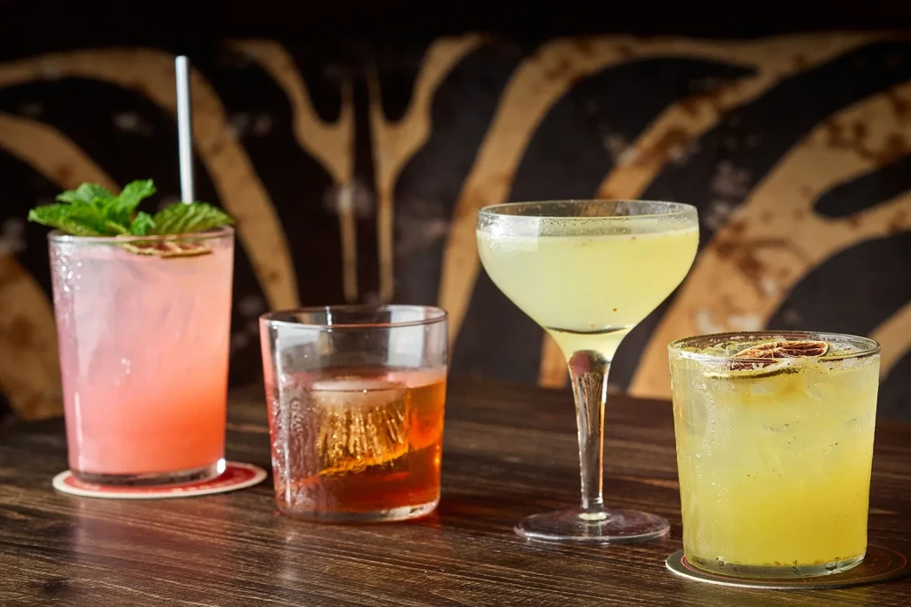 Four distinct cocktails on a wooden surface with a zebra-patterned background.