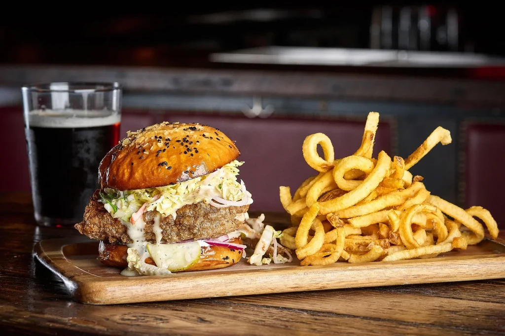 A crispy chicken sandwich, curly fries, and a dark beer.