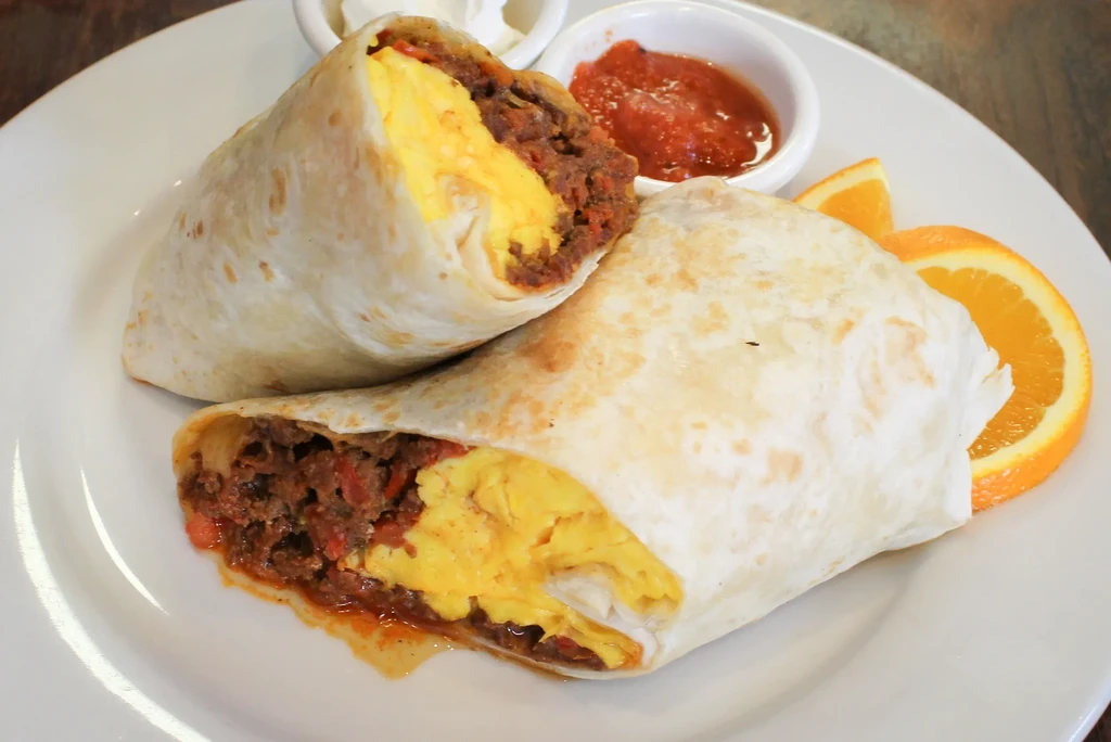 Two burritos filled with scrambled eggs and chorizo, with salsa and orange slices.