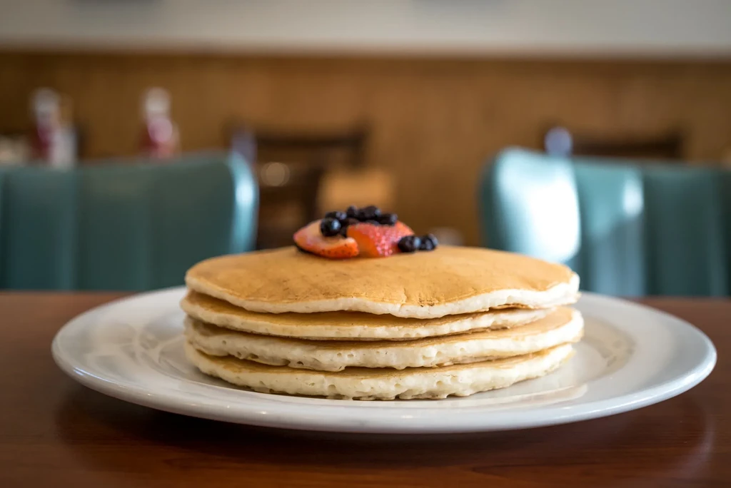 Stack of pancakes with strawberries and blueberries on a diner table.