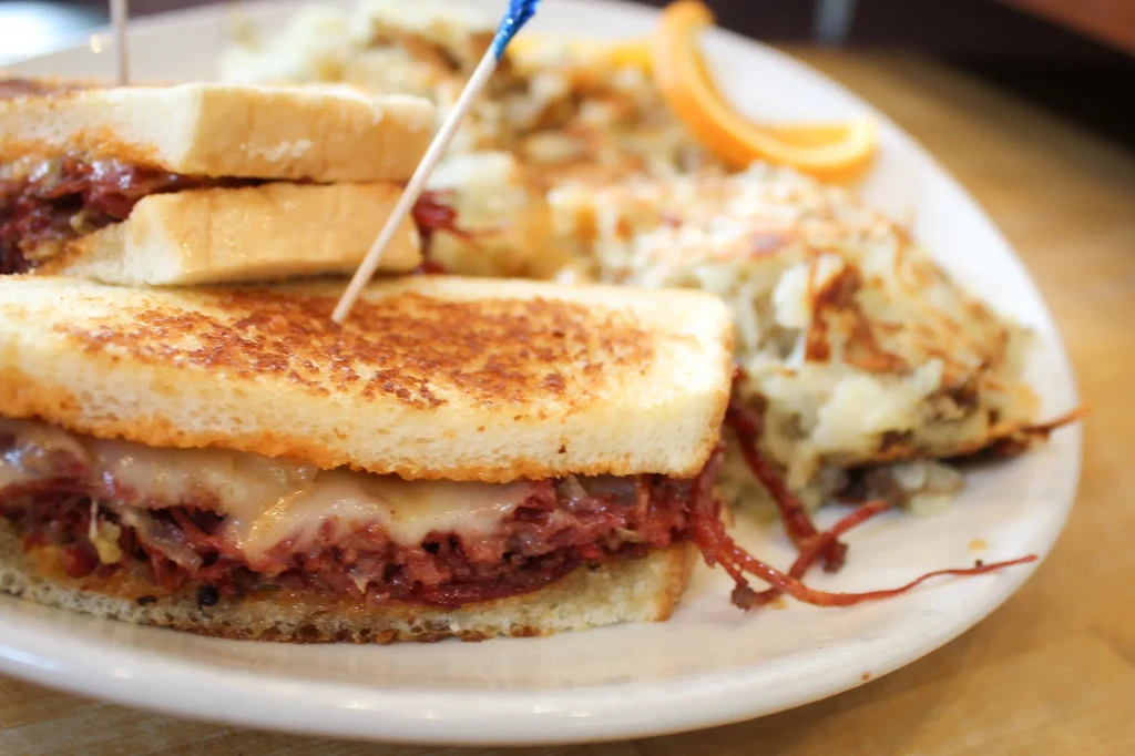 Grilled sandwich with melted cheese and meat, hash browns, and an orange slice.