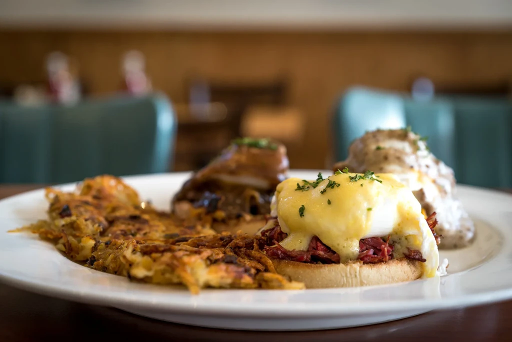 A plate of eggs Benedict, hash browns, and another dish.