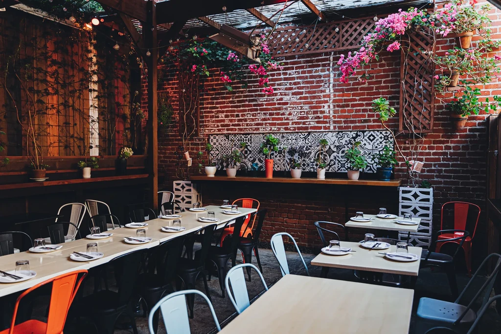 An empty, vibrant outdoor restaurant patio with brick walls and plants.