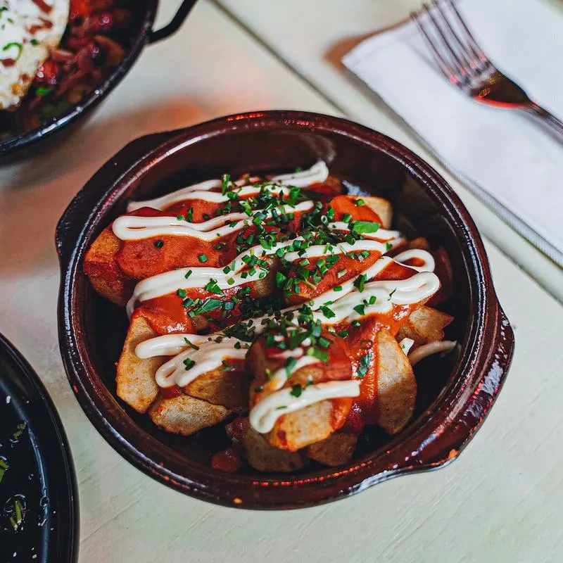 A bowl of patatas bravas with red sauce, aioli, and chives.