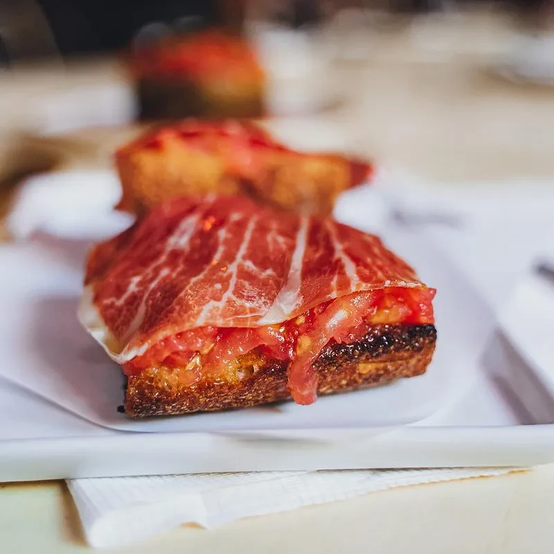 Toasted bread with tomato and slices of prosciutto on a white tray.