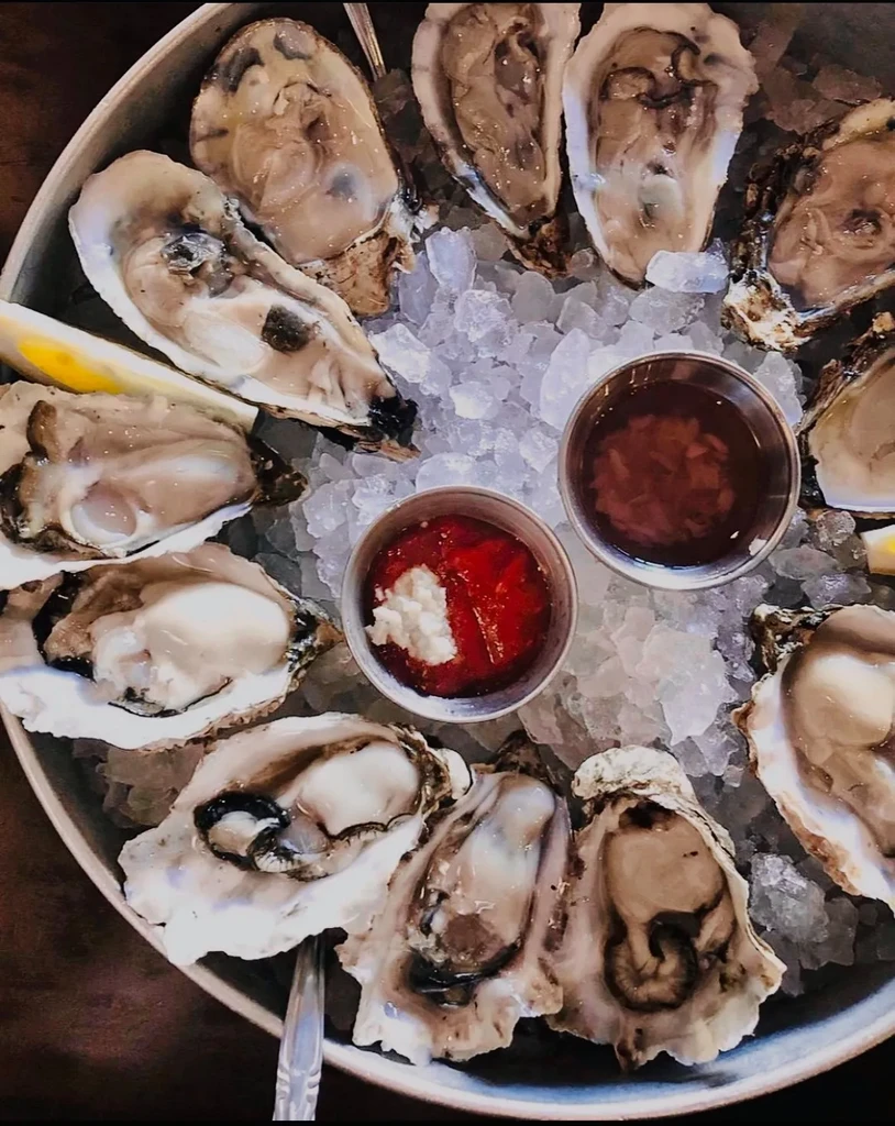 A dozen fresh oysters on ice with lemon and dipping sauces.