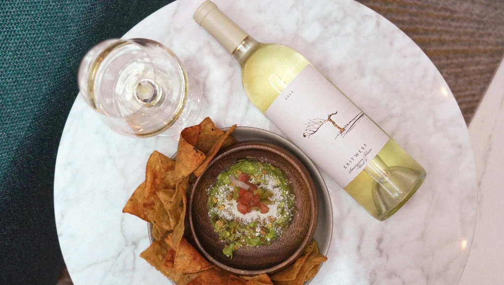 Overhead view of a glass of wine, white wine bottle, and guacamole with chips.