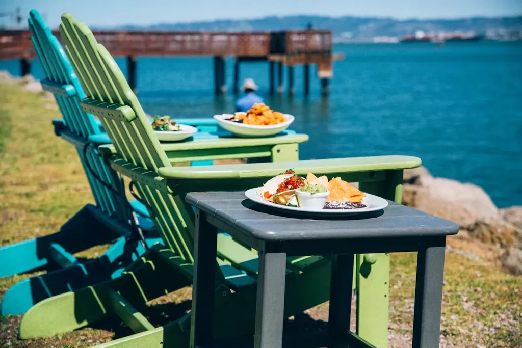 Food and drinks on Adirondack chairs by the blue ocean.