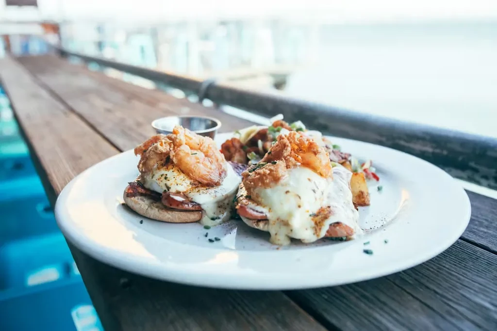 Shrimp and eggs benedict on a white plate on a wooden table.