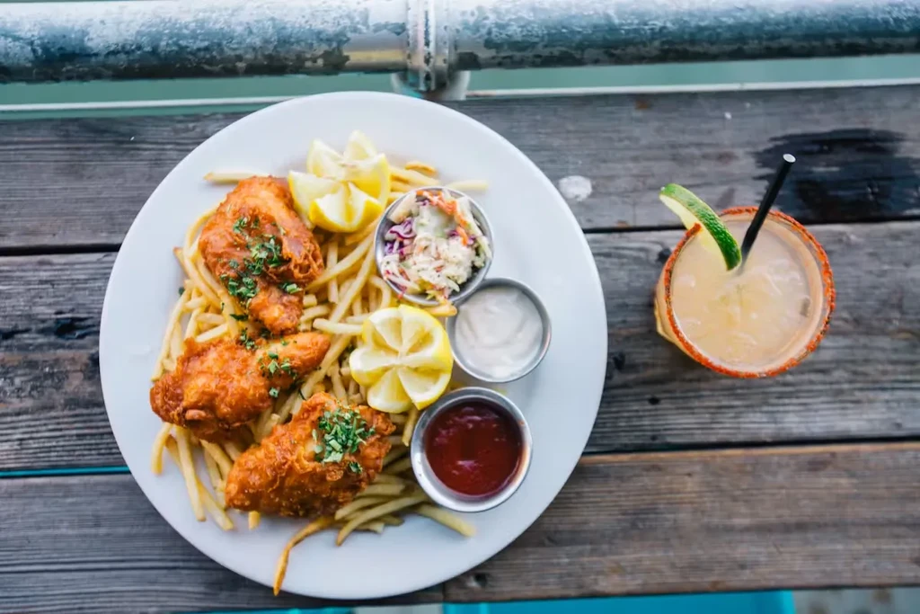 Fried fish and fries with sauces, coleslaw, and a cocktail.