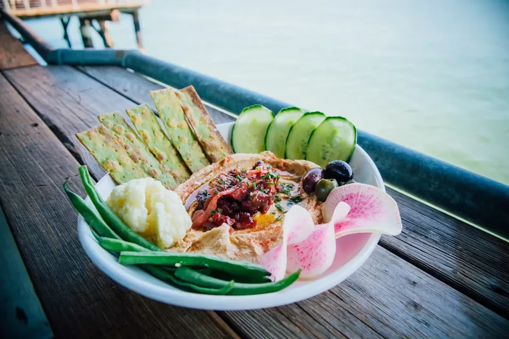 Hummus plate with vegetables and crackers on a wooden dock.