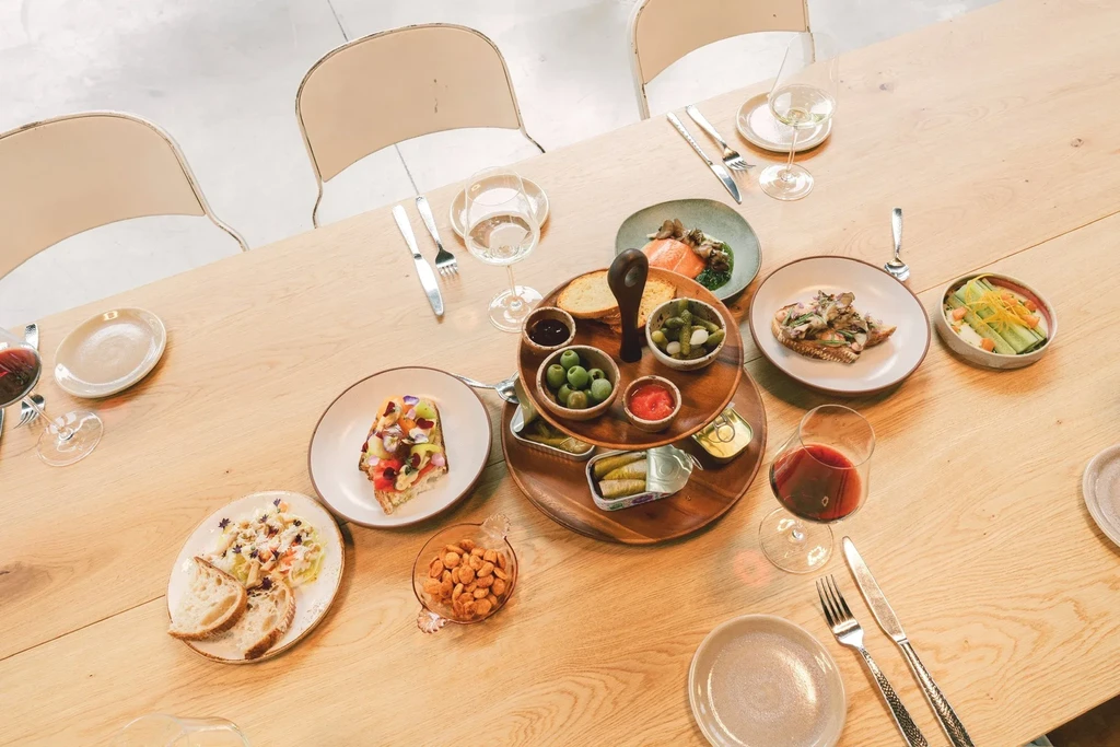 A wooden table laden with various dishes, snacks, and wine glasses.