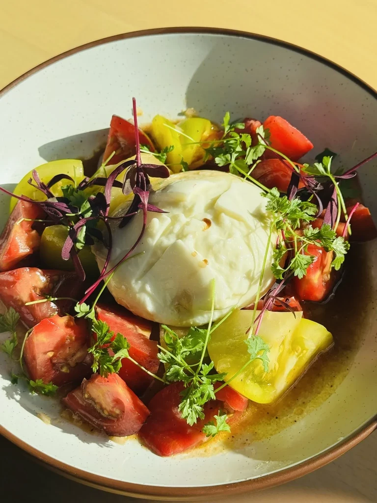 A bowl of burrata cheese and sliced red and yellow tomatoes.