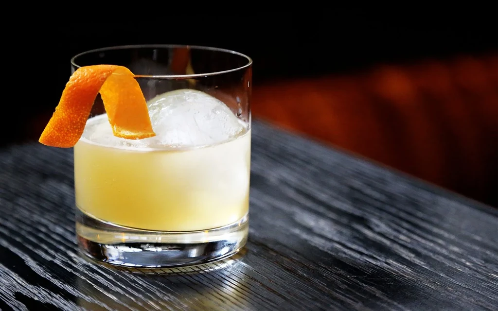 A short cocktail with ice and orange peel garnish on a dark wooden table.