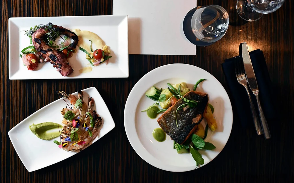 Overhead view of three plates of gourmet food on a dark table.