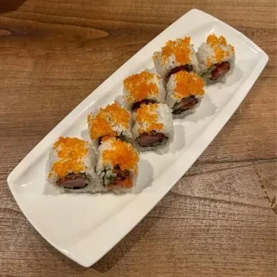Eight sushi rolls with orange roe on a white platter.