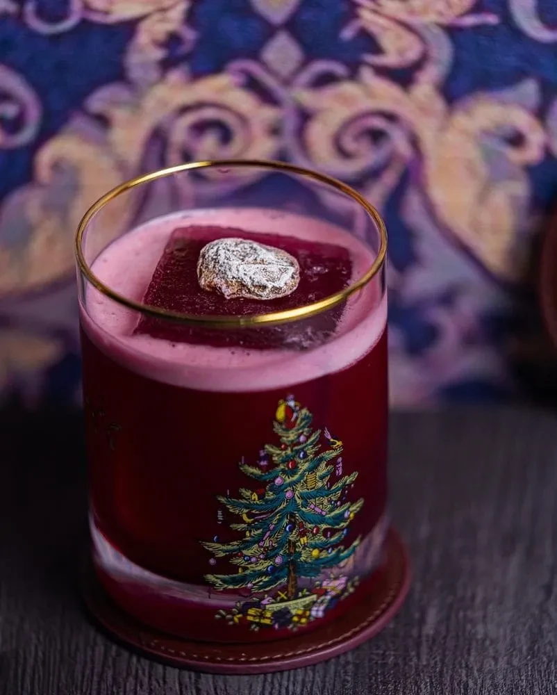 A festive red cocktail in a Christmas tree-decorated glass with a candied garnish.