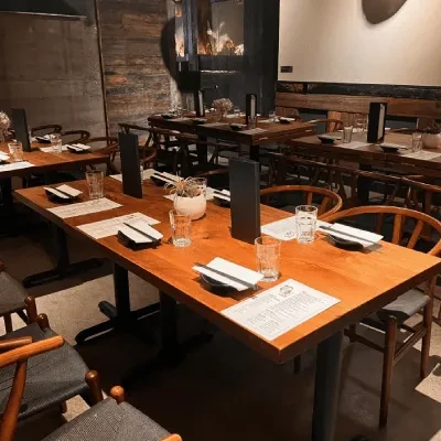 Empty restaurant dining room with wooden tables, chairs, and place settings.