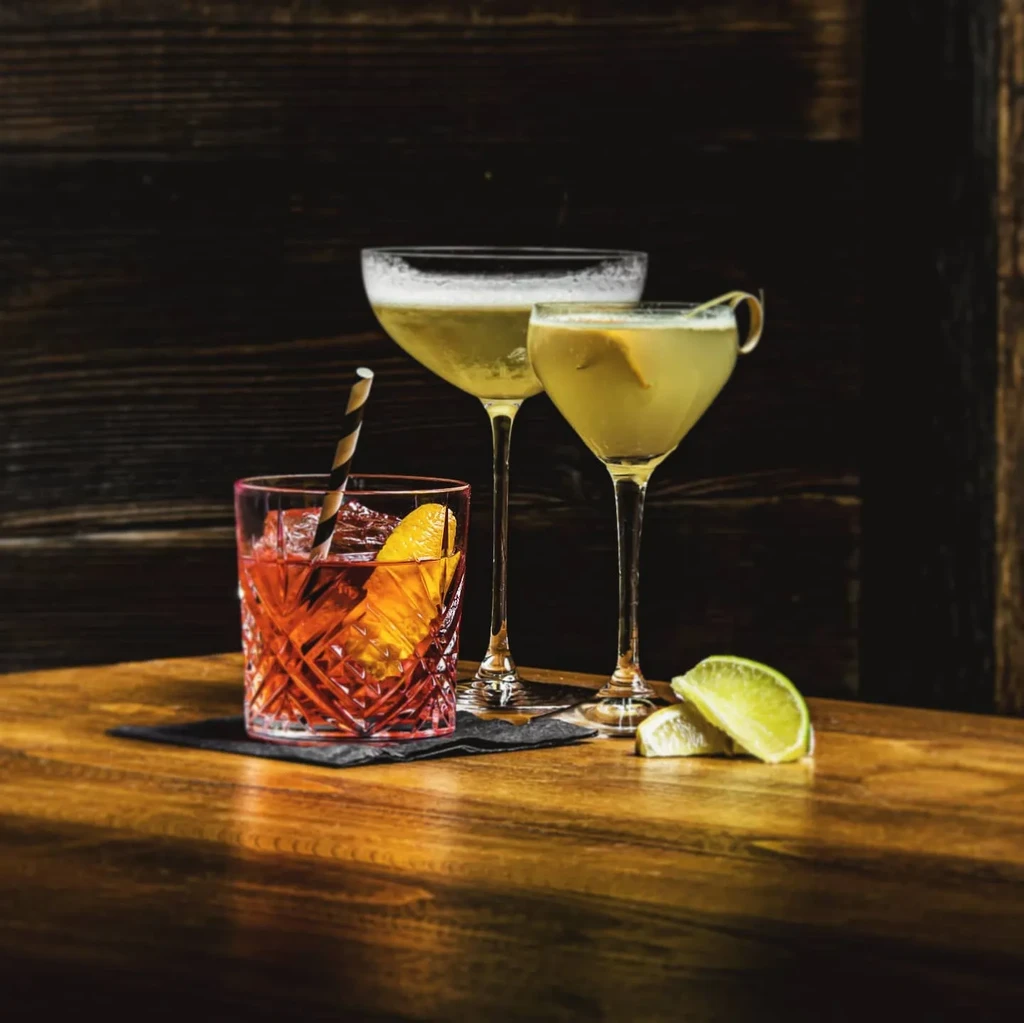 Three cocktails on a wooden table with lime wedges.