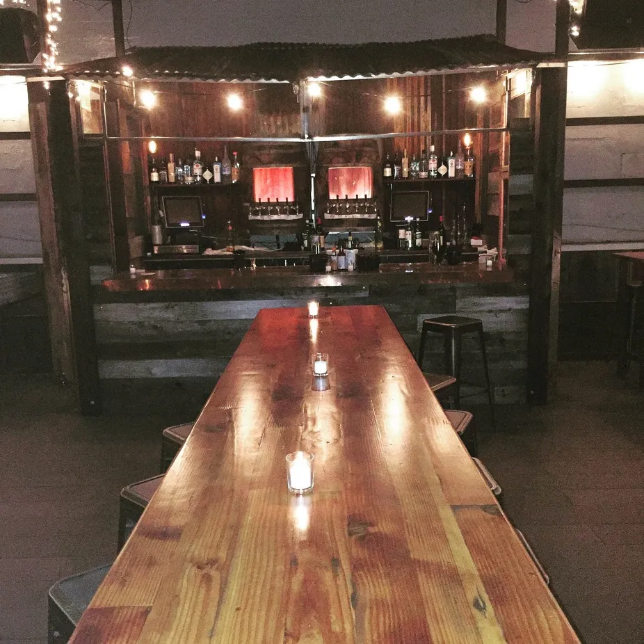 Empty bar interior with long wooden table and lit candles.