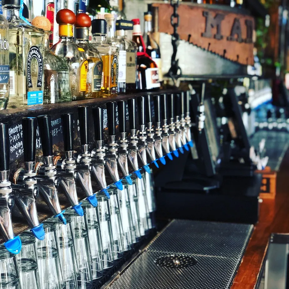 Row of beer taps, liquor bottles, and glasses at a bar.