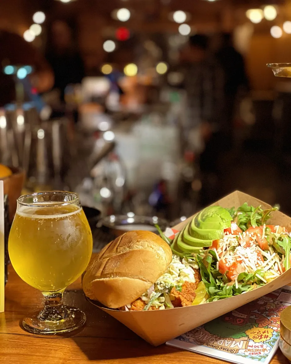 Beer, fried chicken sandwich, and salad on a bar table.