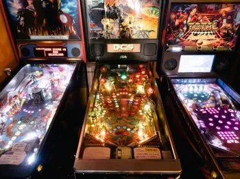 Three brightly lit pinball machines lined up side-by-side.