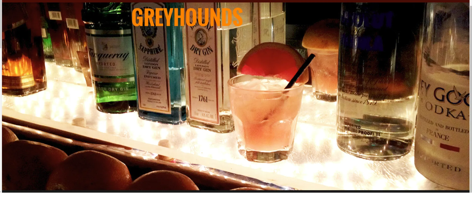Greyhound cocktail, gin and vodka bottles on a lit bar.