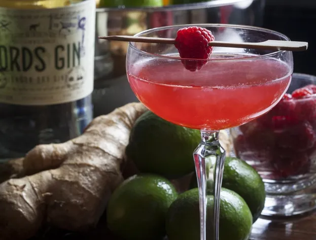 Pink cocktail with raspberry, Lords Gin bottle, ginger, and limes.