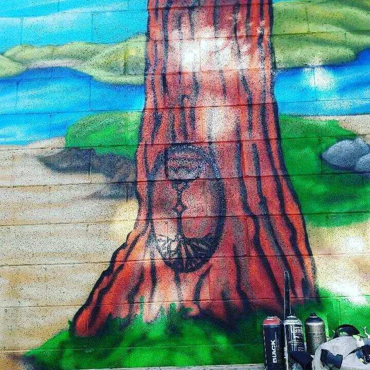 Spray paint mural of a tree trunk and circular symbol on brick wall.