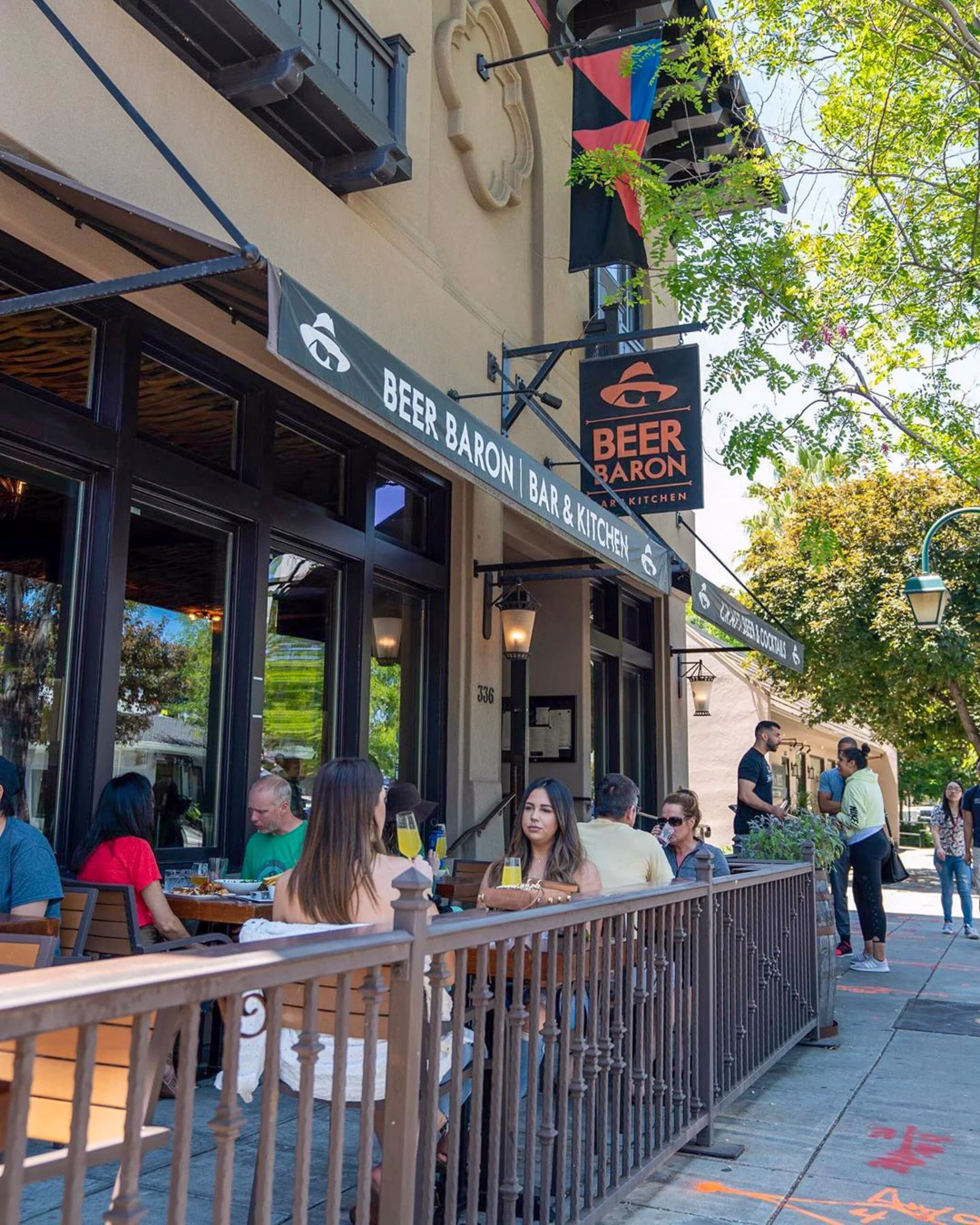 People dining outdoors at Beer Baron Bar & Kitchen on a sunny day.