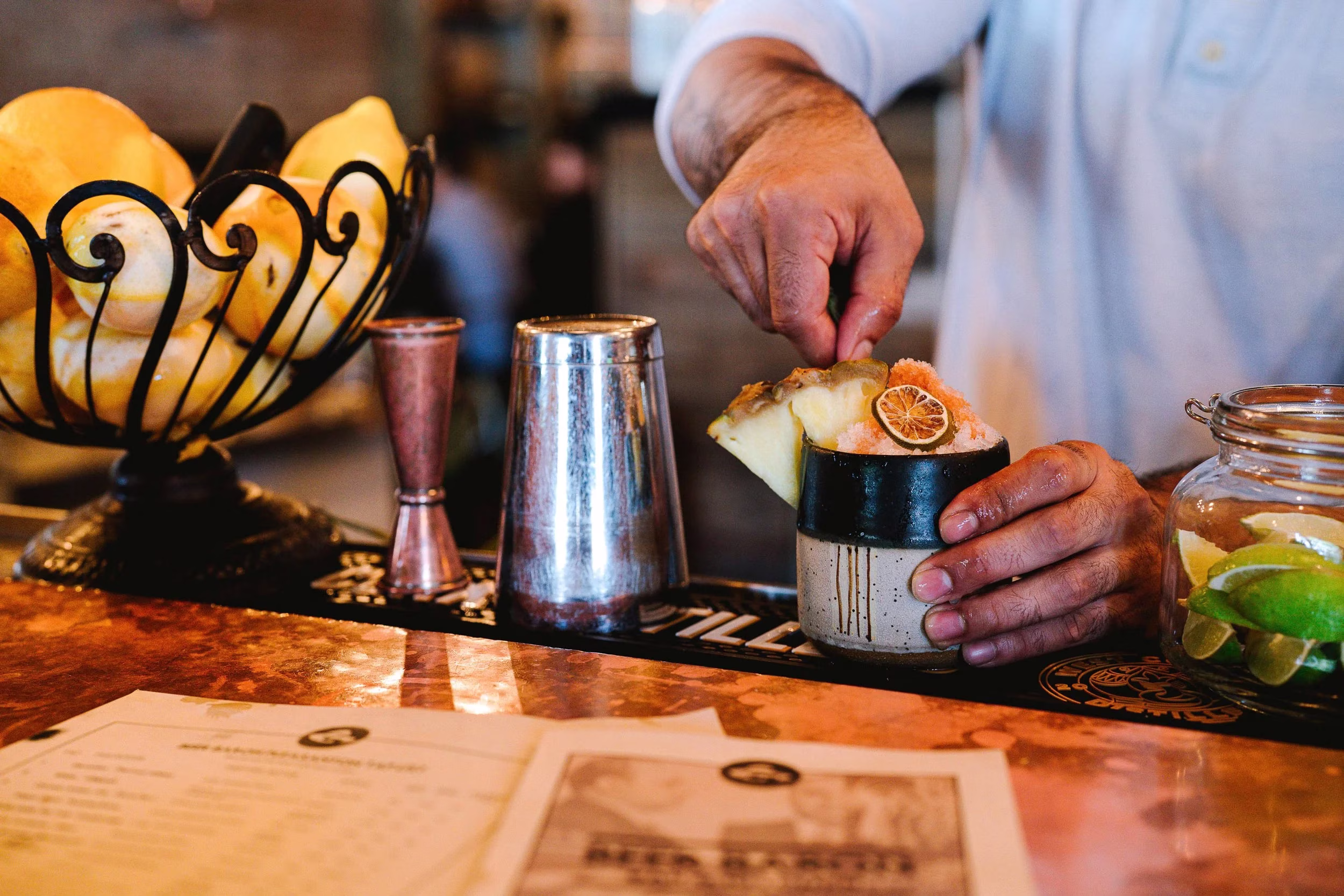 Bartender's hands garnishing a cocktail with fruit and crushed ice.
