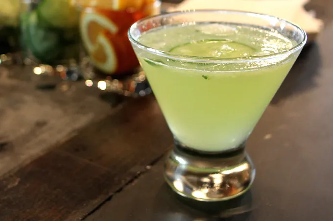 Light green drink with cucumber slices in a martini glass.