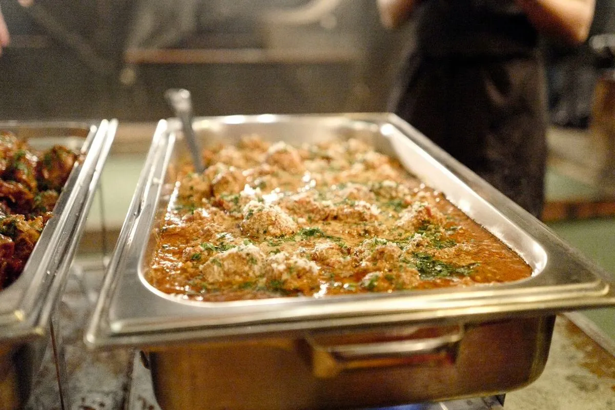 Buffet tray filled with meatballs, tomato sauce, cheese, and herbs.