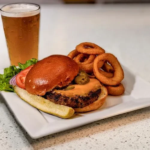 A cheeseburger, onion rings, pickle spear, and a glass of beer.