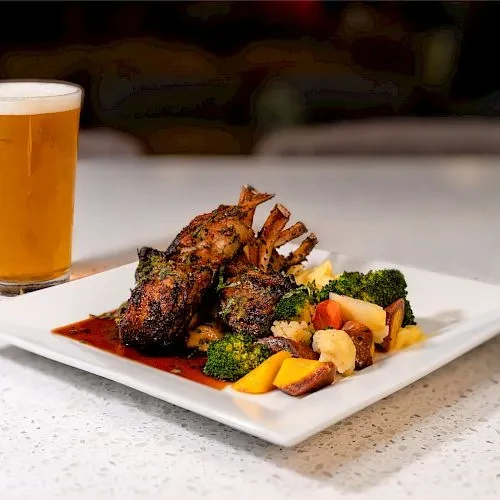 Rack of lamb with vegetables and a glass of beer.