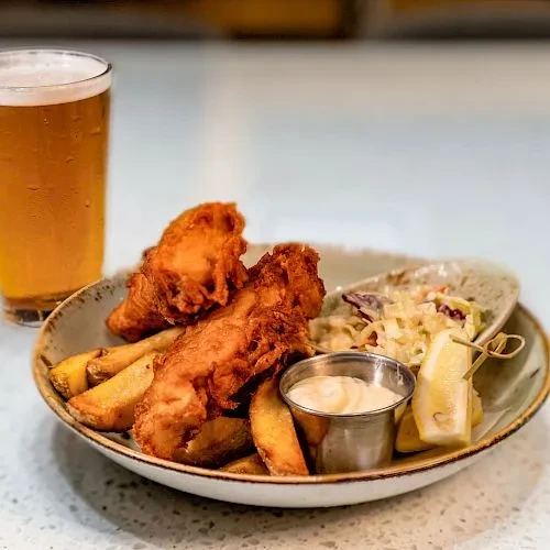 Fish and chips with coleslaw, lemon, and a glass of beer.